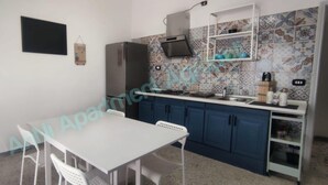 A compact kitchen with a white table and chairs, blue cabinets, and a tiled backsplash.