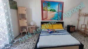 A bedroom with a bed, a wardrobe, a shelf, a ladder, and a painting of a beach scene.