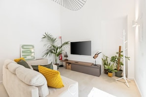 A modern living room with a sofa, a flat-screen TV, a coffee table, and a plant stand.