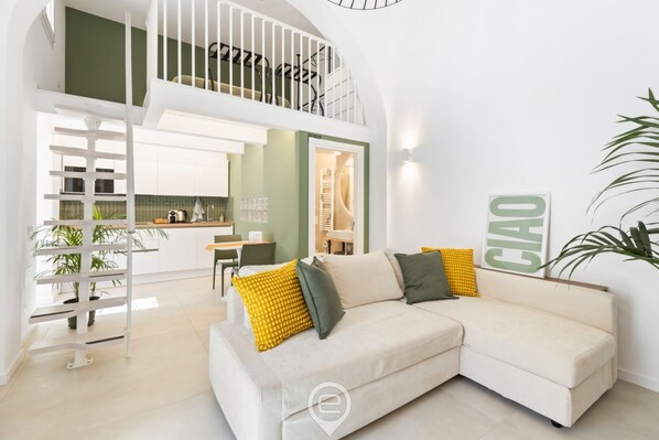 A modern living room with a white sofa, a staircase, and a kitchen area.