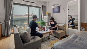 A modern hotel room with a sofa, a small table, a mirror, and a view of the cityscape. - The West Lake Serenity'N Homestay Ha Noi (Hanoi)