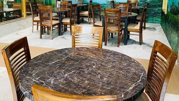 A restaurant with wooden tables and chairs, a ceiling fan, and a mural of a waterfall. - Hotel T2 Grand (Mumbai)