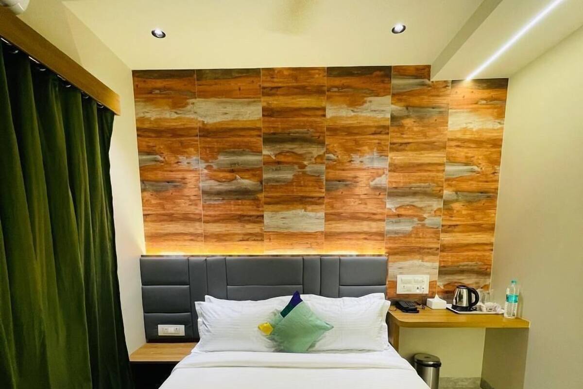 A hotel room with a bed, a nightstand, a desk, and a wall with a wood-like pattern.