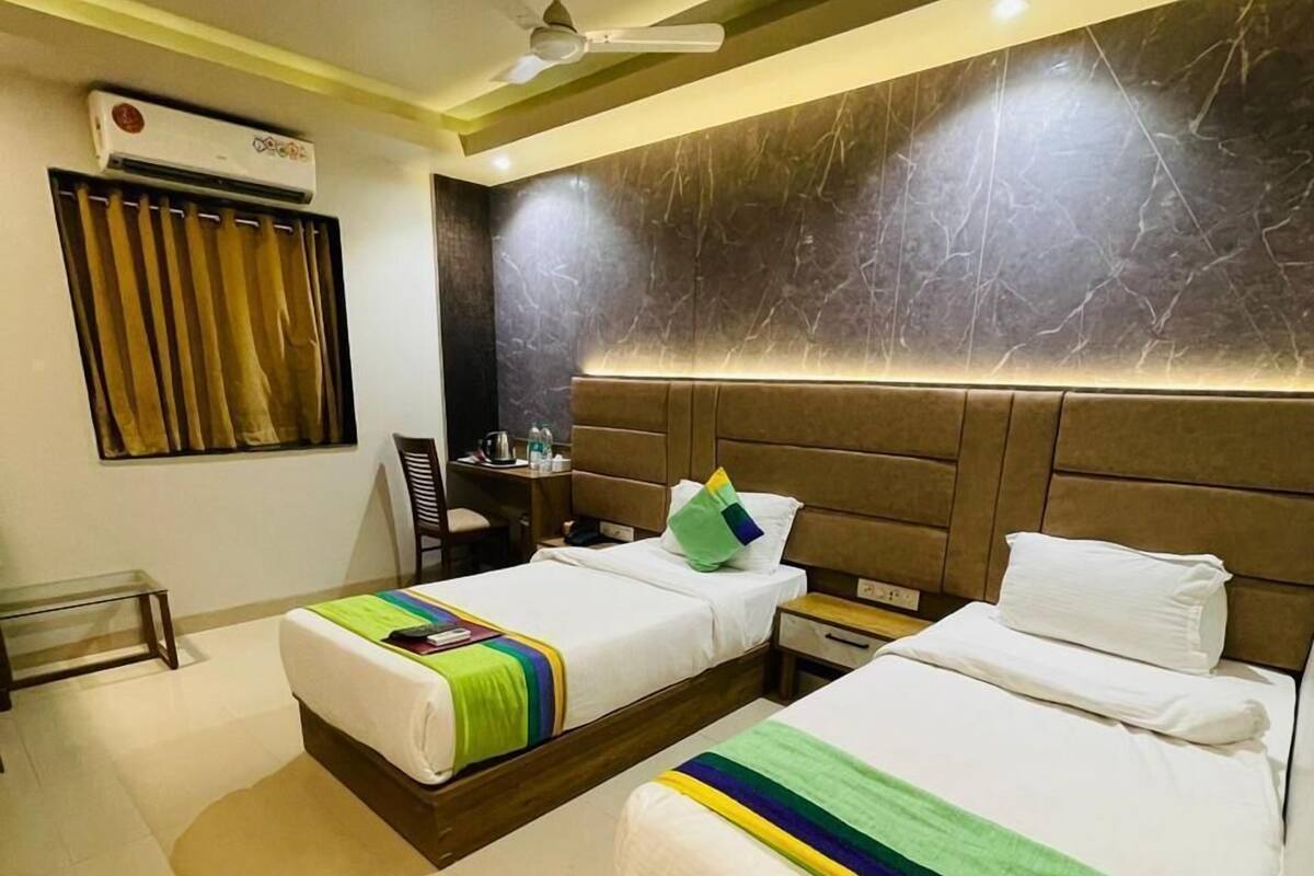 A hotel room with two beds, a ceiling fan, an air conditioning unit, a desk with a chair, and a window with curtains.