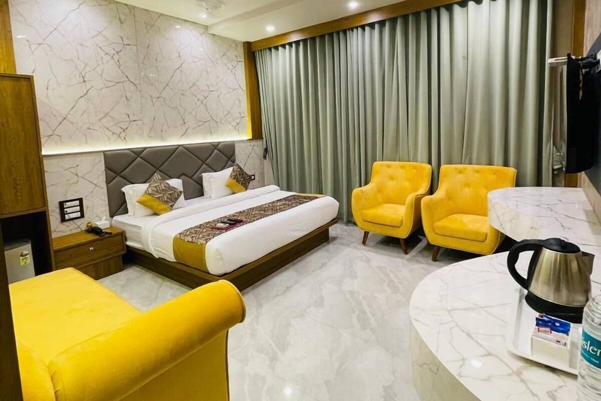 A modern hotel room with a bed, two yellow armchairs, a marble bathroom counter, and a ceiling fan.