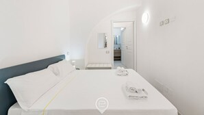 Habitación de hotel moderna con una cama bien hecha, una mesita de noche con artículos de aseo y vistas al baño.