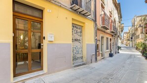Una calle estrecha con un edificio amarillo que destaca por una puerta de madera grande y una ventana con grafiti.