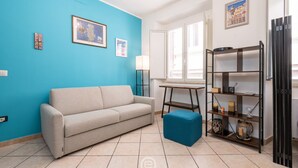 Un soggiorno con una parete blu, un divano beige, un poggiapiedi blu, un tavolino in legno e una scaffalatura nera con diversi oggetti.