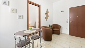 Uma sala de estar moderna com uma mesa de jantar redonda, duas poltronas marrons, uma porta de madeira e um espelho hexagonal fixado na parede.