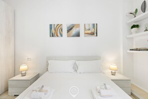 Ein modernes Hotelzimmer mit einem großen Bett, weißer Bettwäsche, zwei Nachttischen mit Lampen und abstrakter Wandkunst.