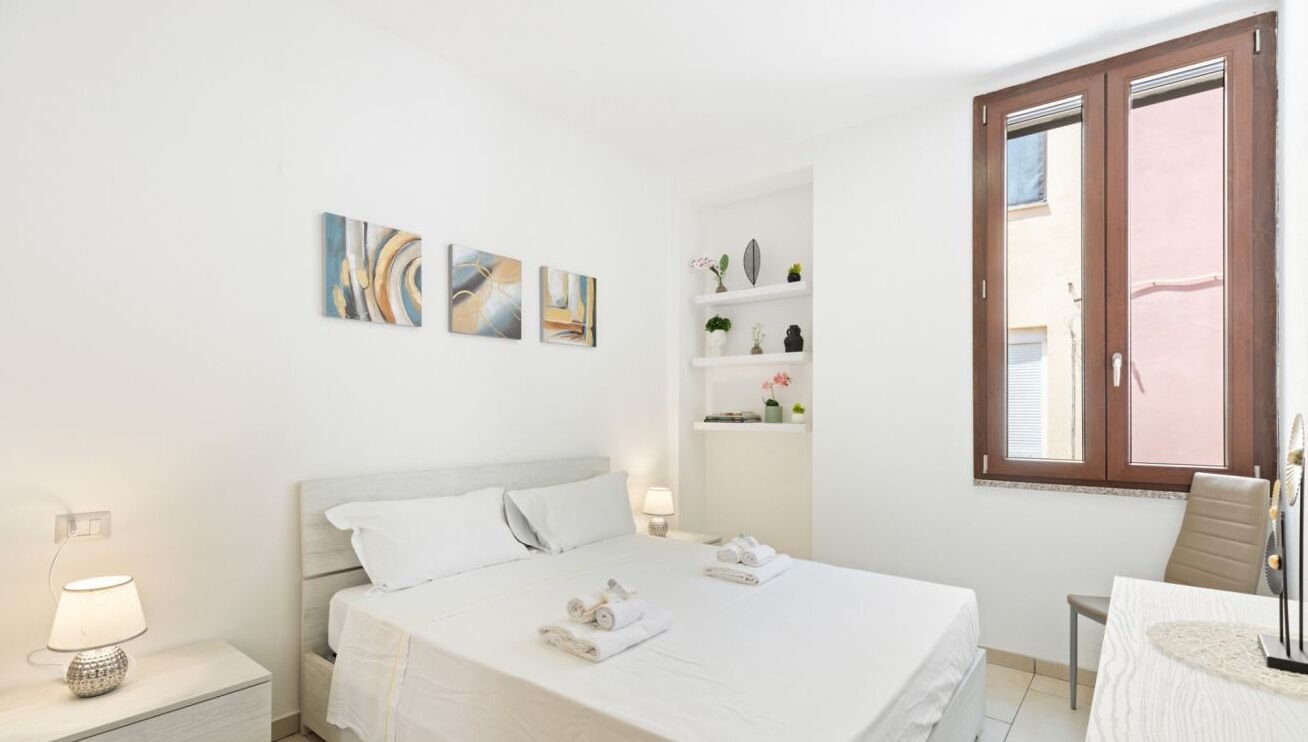 A hotel room with a bed, bedside tables, a chair, a small table, and a window with curtains.