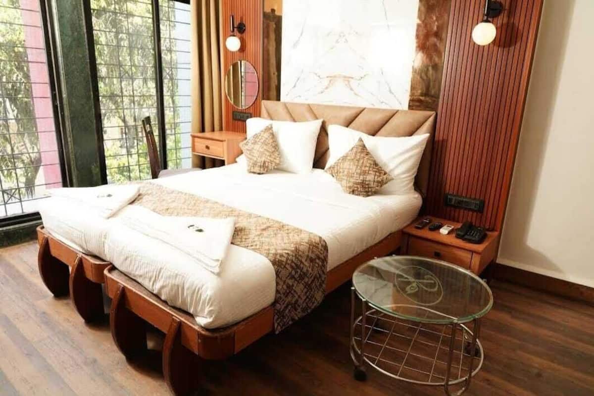 Ein ordentlich bezogenes Bett mit Holzbettrahmen, ein Glastisch und ein Nachttisch mit Telefon und Lampe.