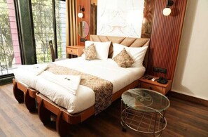 A neatly made bed with a wooden frame, a glass table, and a nightstand with a phone and a lamp. - HOTEL PADMAKRISHNA (Pune)