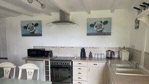A kitchen with a stove, microwave, toaster, and sink. There are two paintings on the wall and a ceiling light fixture. - Charming 1-bedroom gite in delightful countryside hamlet with views (Saint-Georges-de-Livoye)