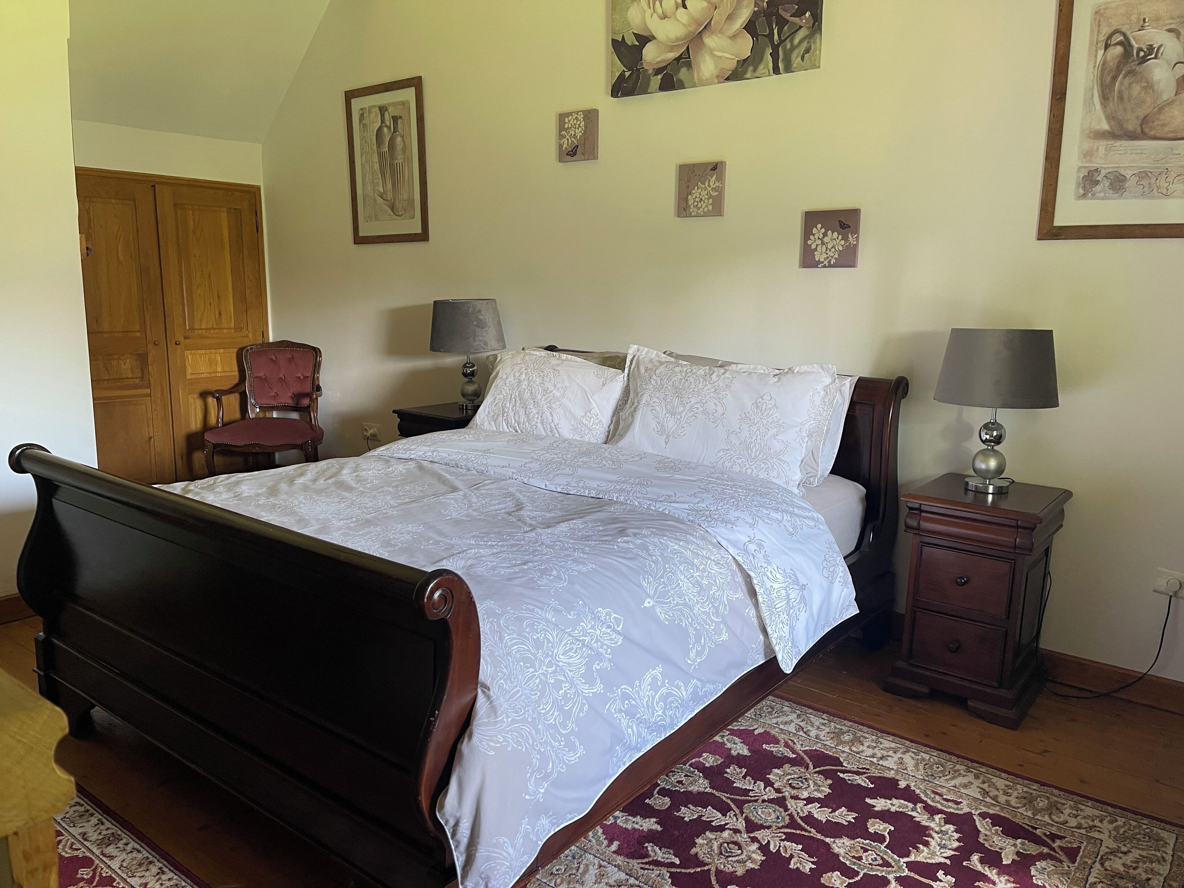 Un dormitorio con una cama de madera, dos mesitas de noche con lámparas, una silla y una puerta.