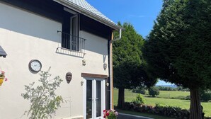 A house with a balcony, a clock, and a large window. - Charming 1-bedroom gite in delightful countryside hamlet with views (Saint-Georges-de-Livoye)