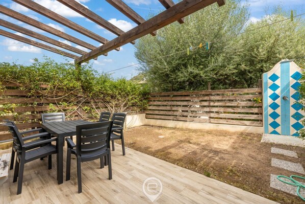 Un patio al aire libre con una pérgola de madera, una mesa y sillas, y una valla de madera.