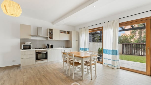 A modern kitchen with white cabinets, a wooden dining table, and a large sliding glass door leading to a balcony.