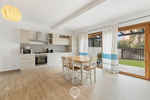 Eine moderne Küche mit weißen Schränken, einem Holztisch und einer großen Schiebeglastür, die auf einen Balkon führt.