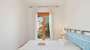A bedroom with a bed, a nightstand, a lamp, and a view of a building and trees through a window.