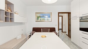 Una cocina moderna con armarios blancos, una mesa de comedor con sillas, un cuadro en la pared y vistas a otra habitación.