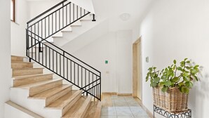 Una escalera con escalones de madera y barandillas negras, que conduce a una habitación con paredes blancas y suelo de baldosas.