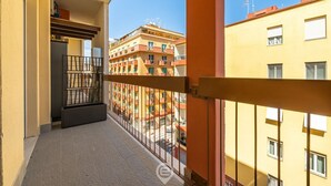 Ein schmaler Balkon mit Metallgeländer, eine Tür zu einem Zimmer und Blick auf angrenzende Gebäude.