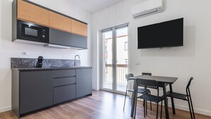 Eine moderne Küche mit grauen Schränken, einer schwarzen Mikrowelle und einem eingebauten Backofen. Es gibt einen Essbereich mit Tisch und Stühlen, sowie einen großen Flachbildfernseher an der Wand.