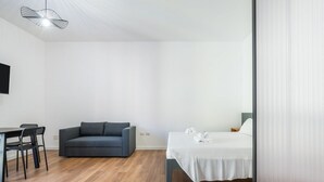 Ein Zimmer mit einem Bett, einem Schlafsofa, einem Esstisch mit Stühlen und einem Fernseher an der Wand.