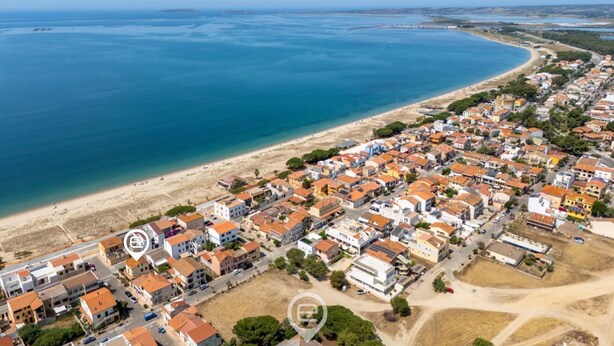 Una vista aerea di una cittadina costiera con una spiaggia, case dai tetti rossi e un mare blu cristallino.