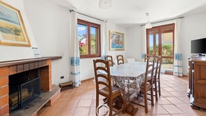 Zona pranzo con camino, sedie di legno, un tavolo e ampie finestre con tende.