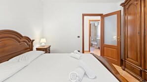 Una camera d'albergo con un letto in legno, un comodino con una lampada, un armadio e un bagno visibile tramite una porta aperta.