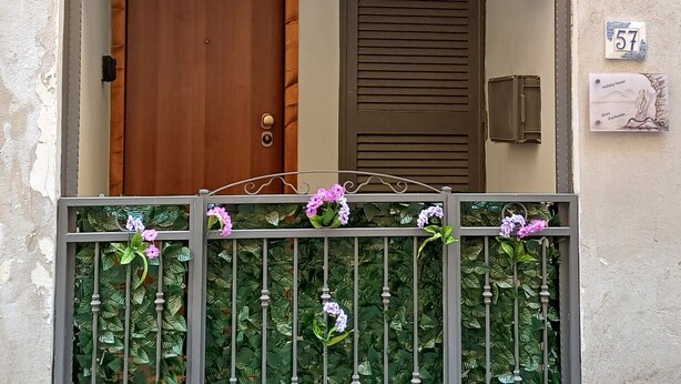 A building entrance with a wooden door, a metal gate with flowers, and a number plaque.