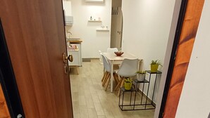 A hallway leading to a dining area with a wooden floor, a dining table with chairs, and a small plant on a side table.