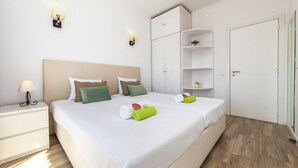 A neatly arranged bedroom with a large bed, bedside tables, a wardrobe, and a door. - Penthouse San Lorenzo (Portimão)