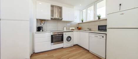 A modern kitchen with white cabinets, a stainless steel range hood, a washing machine, and a dishwasher.