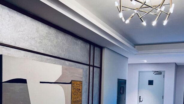 A hallway with a modern design, featuring a large abstract artwork on the wall, a contemporary light fixture, and a door at the end. - Apartment 2 in Zed Towers (El Sheikh Zayed City)