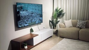 A modern living room with a flat-screen TV mounted on the wall, a sofa, a coffee table, a potted plant, and a large rug. - Apartment 2 in Zed Towers (El Sheikh Zayed City)