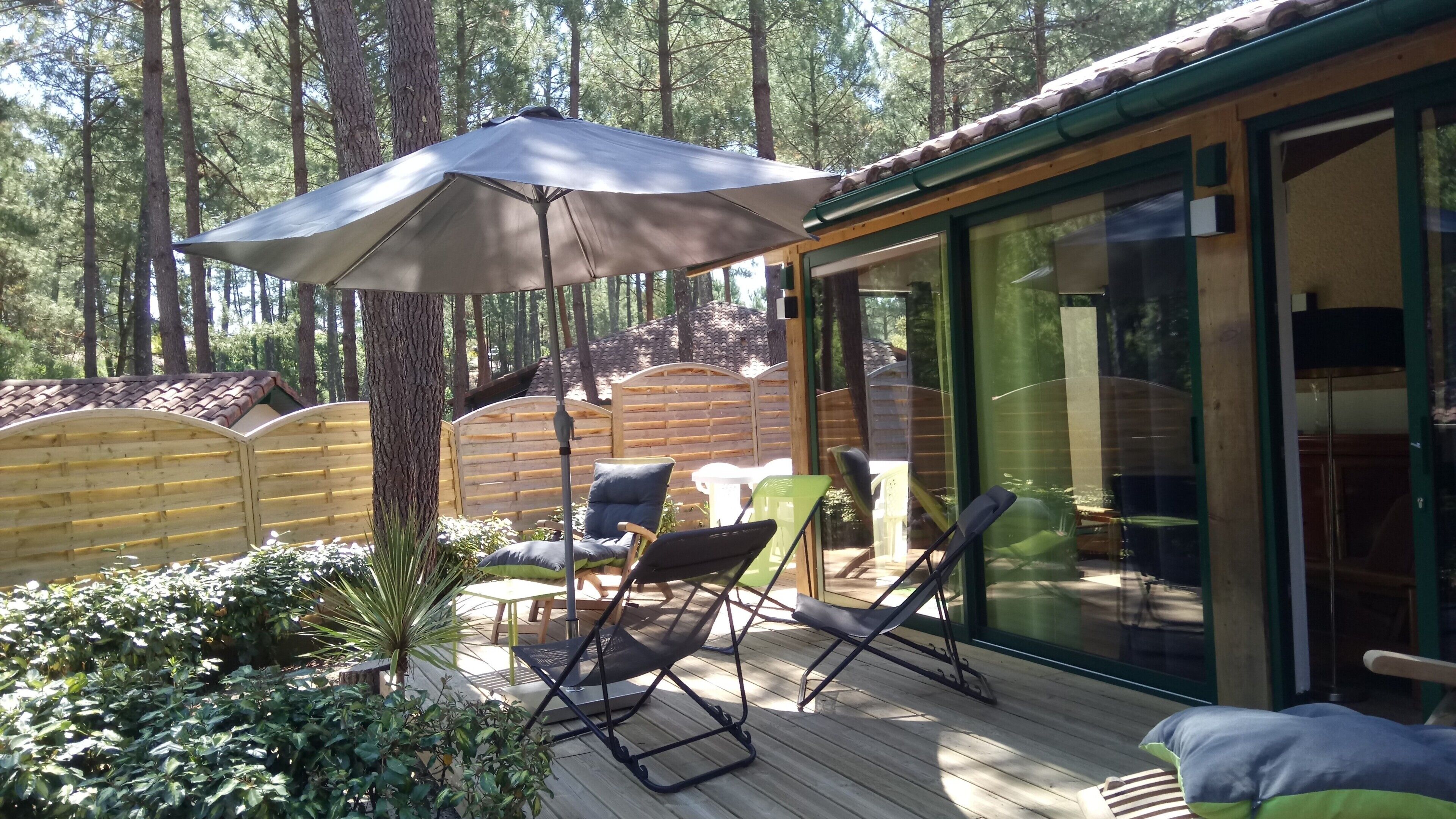 Une terrasse dotée de mobilier d’extérieur, d’un grand parasol et d’une porte vitrée donnant sur un espace abrité.