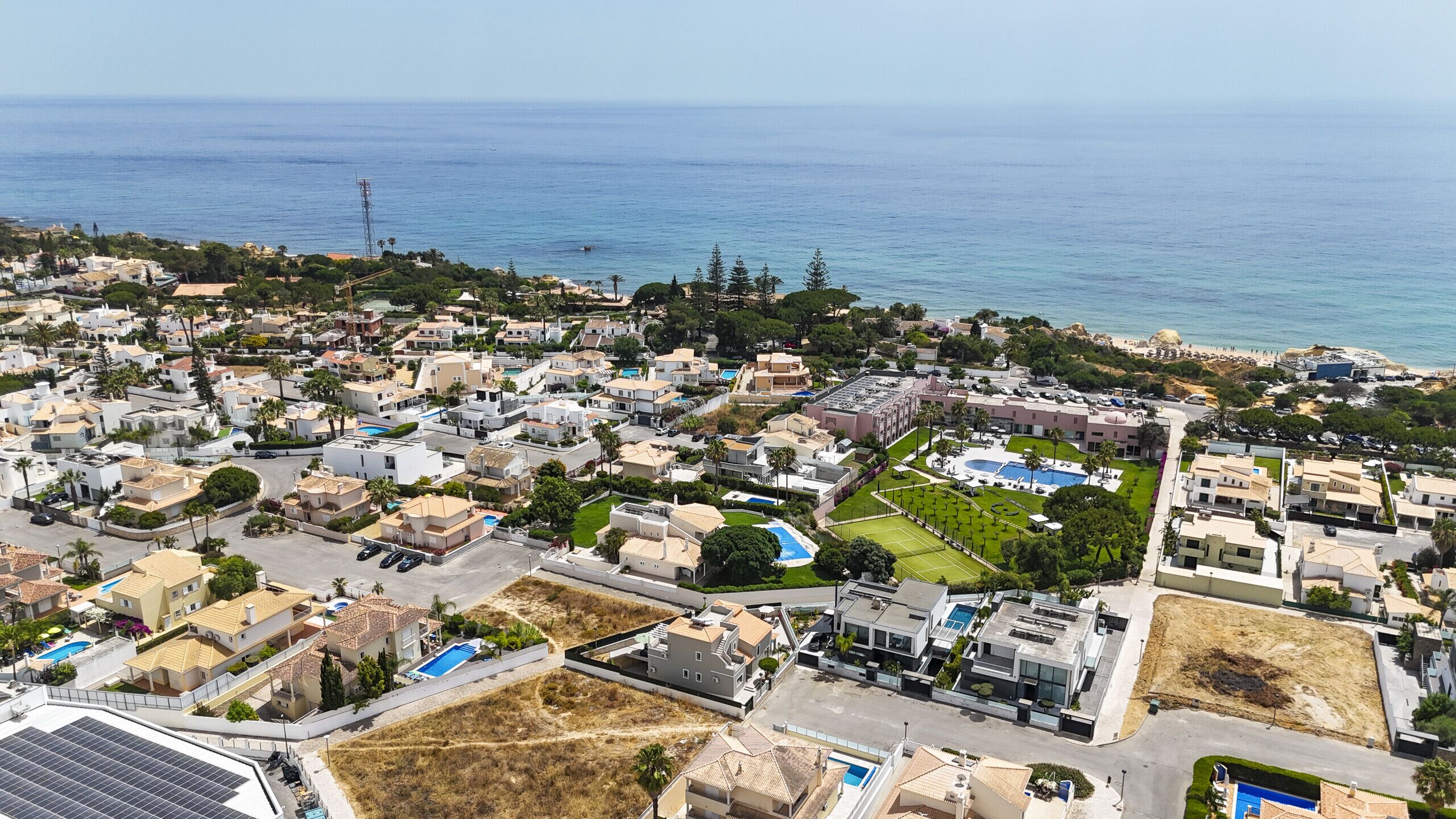 An aerial view of a coastal residential area with houses, a swimming pool complex, and a beach.