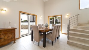A dining area with a marble table, six chairs, a wooden cabinet, and a staircase. - Villa Gale Coast in Gal (Albufeira)
