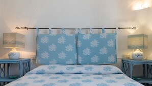 Una cama con una colcha azul y blanca, dos almohadas a juego y un cabecero con una barra metálica. Hay dos mesitas de noche con lámparas y objetos decorativos.