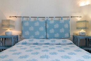 A bed with a blue and white bedspread, two matching pillows, and a headboard with a metal rod. There are two bedside tables with lamps and decorative items. - Villa Panta Rei - Liscia di Vacca (Liscia di Vacca)