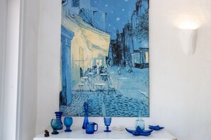 A painting of a street scene with buildings and people, displayed above a shelf with blue glassware. - Villa Panta Rei - Liscia di Vacca (Liscia di Vacca)