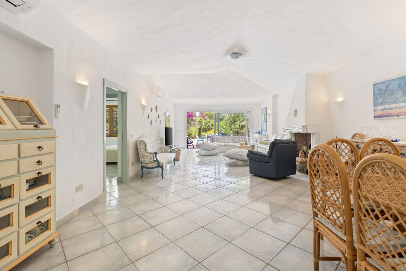 A spacious living area with a high ceiling, a dining set, and a view through a glass door to the outdoors.