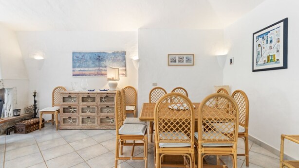 Un comedor con sillas de mimbre y una mesa de madera, un aparador con cajones y un cuadro en la pared.