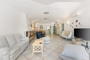 A spacious living area with a sofa, armchairs, a small table, and a television. - Villa Panta Rei - Liscia di Vacca (Liscia di Vacca)