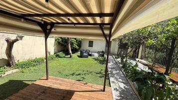 A covered patio area with a wooden deck, a small lawn, and various potted plants.