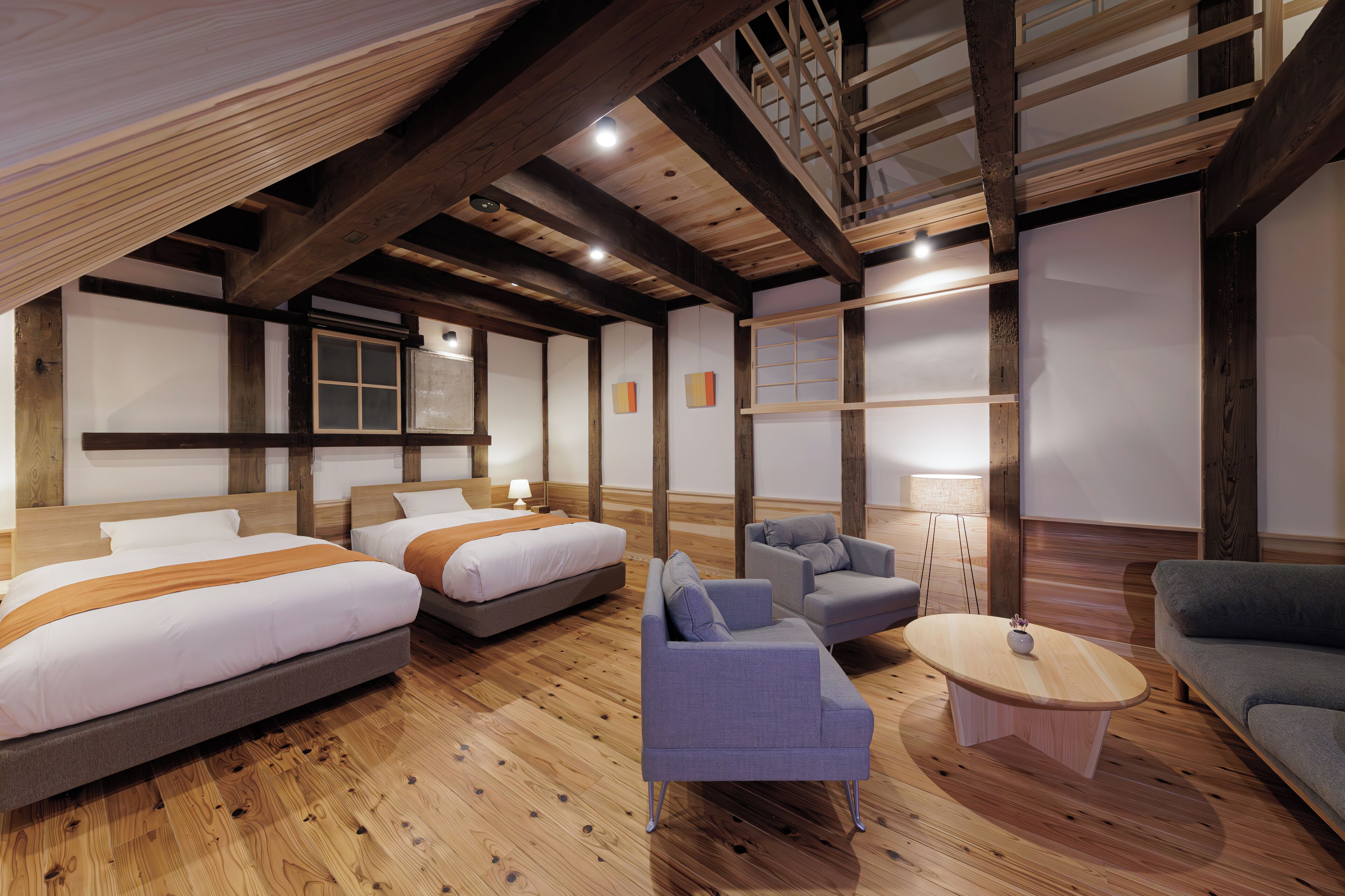 Une chambre d’hôtel moderne avec un plancher en bois, un lit en mezzanine, deux canapés, une table basse et une petite table sur laquelle est posé un vase.