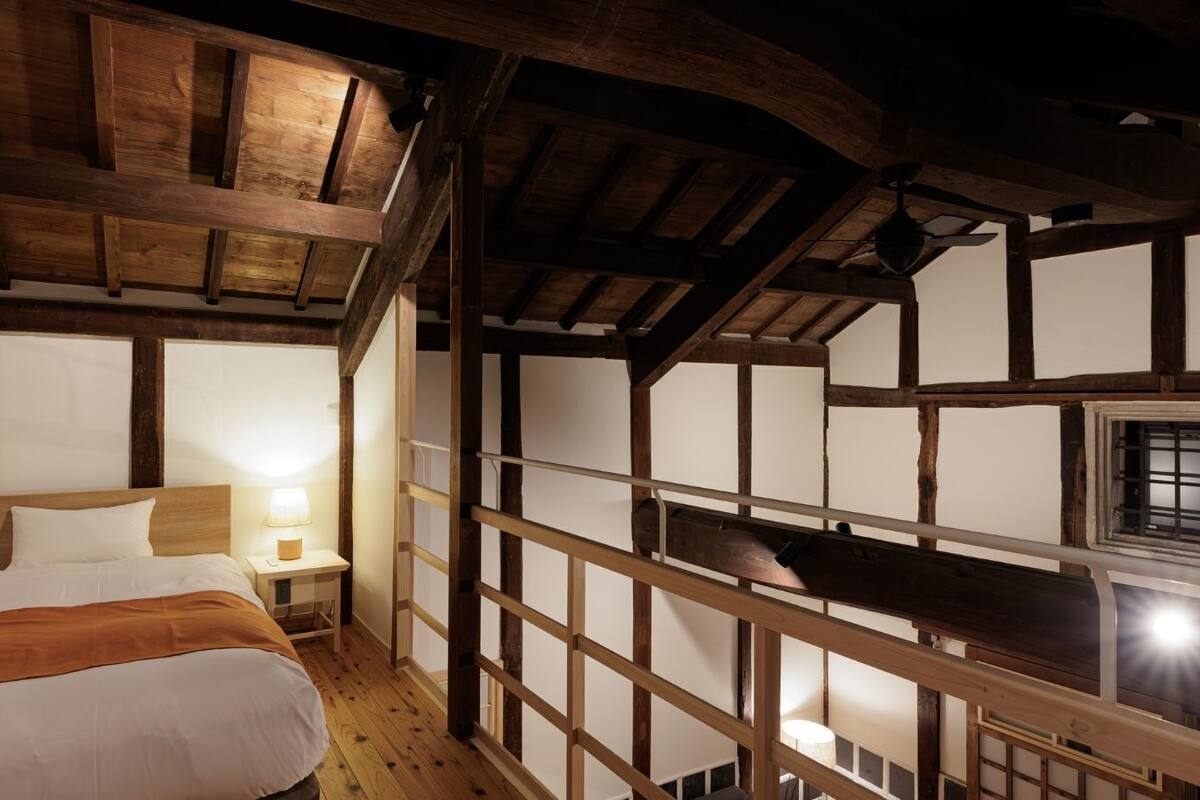 Une chambre avec un plafond en bois, un lit avec une literie blanche, une table de chevet avec une lampe et une fenêtre donnant sur un beau paysage.
